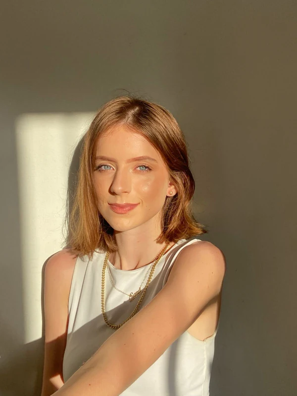 Retrato de Sara com blusa clara, colar dourado e luz de fim de tarde