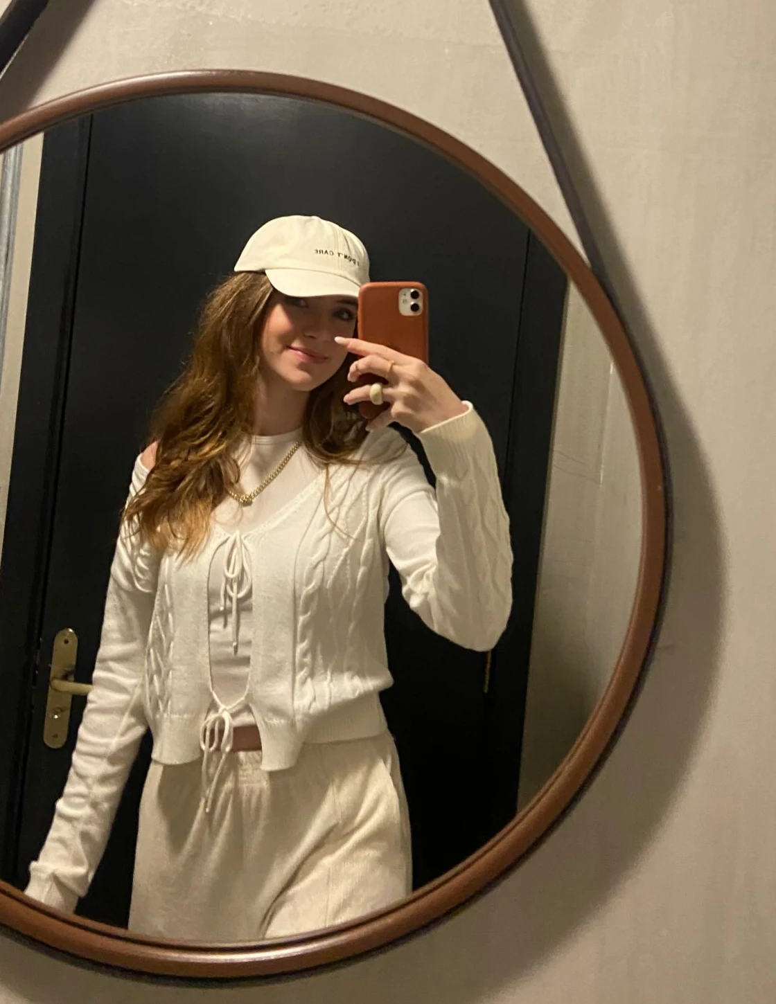 Sara fotografando no espelho um look em off-white com boné e calça clara
