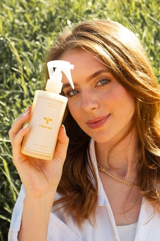 Sara com um produto de cabelo em frasco claro, ao ar livre
