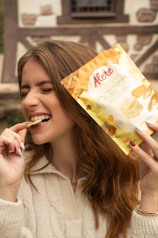 Sara provando um biscoito Alere e segurando a embalagem amarela
